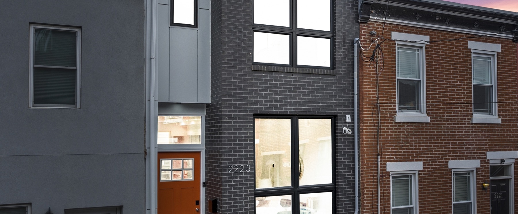 A newly built rowhome on Oakford Street in Point Breeze at dusk, between older brick neighbours